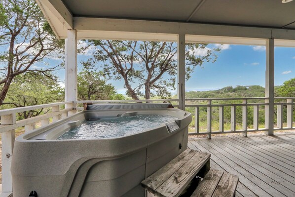 A hot tub on a wooden deck with a view of trees and hills.