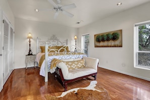 A bedroom with a bed, a sofa, a ceiling fan, a painting, and a window.