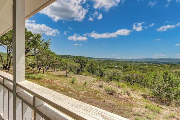 A balcony with a view of a grassy landscape and trees under a clear sky.