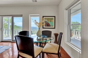 Un coin repas avec une table en verre, des chaises et un vase rempli de fleurs. Deux portes donnent sur un balcon avec vue.