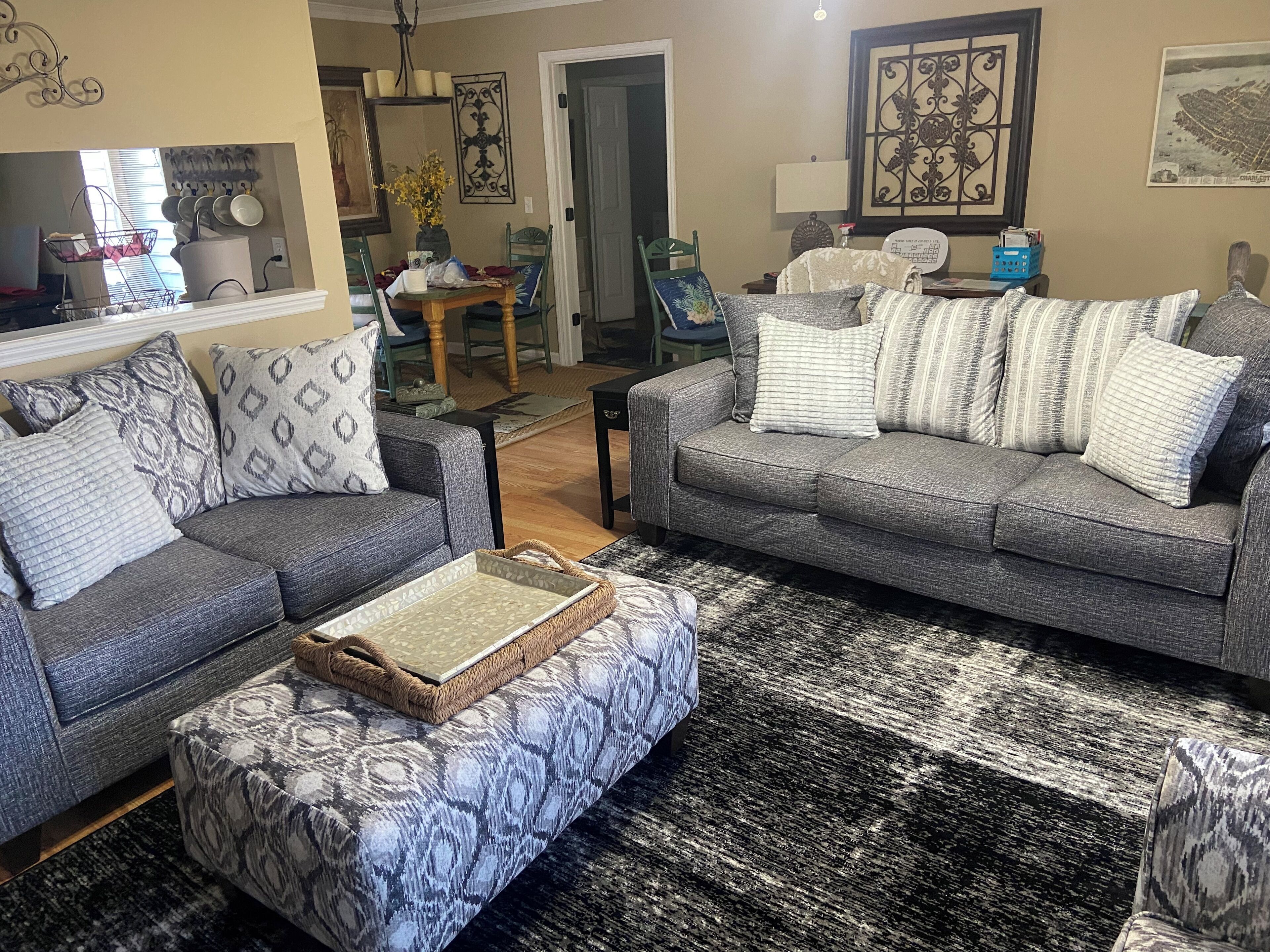 Un salon avec deux canapés gris, des coussins à motifs, un pouf en osier et un tapis noir et blanc.