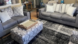 A living room with two grey sofas, patterned cushions, a woven ottoman, and a black and white rug. - Spacious - Private 2 brs, 2 baths (Charleston)