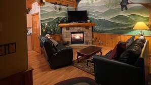 A cozy living room with a fireplace, wooden furniture, and a mural of bears on a tree. - THE ONLY THING MISSING  YOU!Hot tub,air hockey,pool,no animals no smoking sleep6 (Pigeon Forge)