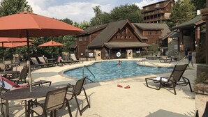 A pool area with lounge chairs and umbrellas, surrounded by wooden buildings with a ski lift visible in the background. - THE ONLY THING MISSING  YOU!Hot tub,air hockey,pool,no animals no smoking sleep6 (Pigeon Forge)