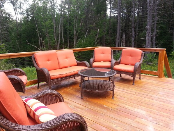 A wooden deck with wicker furniture, including a sofa and chairs, and a small table.
