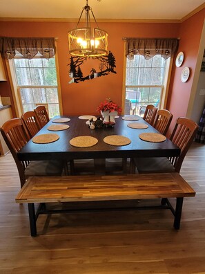 Une salle à manger avec une table en bois, des chaises, un banc, un lustre et un élément décoratif mural.