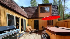 Eine Holzterrasse mit Whirlpool, Sitzgelegenheit und Grill.