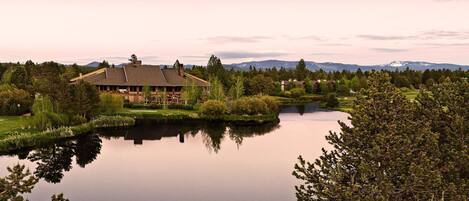 A lodge with a large building surrounded by a lake, trees, and mountains in the background.