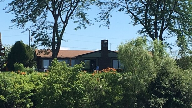 Ein Haus mit braunem Dach und Schornstein, umgeben von dichtem Grün und Bäumen.