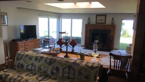 Ein Wohnzimmer mit einer Couch, einem Fernseher, einem Kamin und einem großen Fenster.