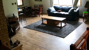 A spacious living room with a wooden floor, a blue sofa, a wooden coffee table, and a dining area with a table and chairs. - Secluded Summer or Winter Getaway! (Island Park)