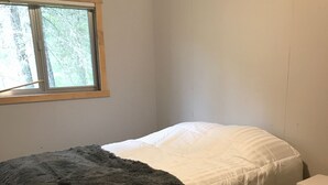 A single bed with a white and gray blanket in a room with wooden flooring and a window. - Secluded Summer or Winter Getaway! (Island Park)