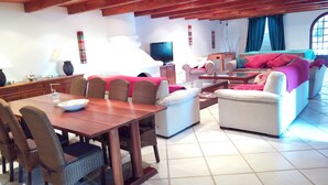 Amplia sala de estar con una mesa de comedor de madera, sillas de mimbre, un sofá y una televisión.