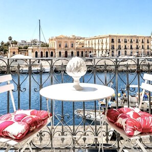A balcony with a table and chairs, overlooking a body of water and a historic building. - Sea-View Loft in Ortigia. Comfort, Style and Unforgettable Sunsets. (Siracusa)