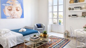 A bright, well-lit room with a bed, a chair, a coffee table, and a large window. - Charming Sea-View Hideaway in Ortigia. Comfort, Style and Unforgettable Sunsets. (Siracusa)