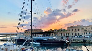 A marina with several boats docked, a building labeled 'DOGAN' in the background, and a sunset sky. - Charming Sea-View Hideaway in Ortigia. Comfort, Style and Unforgettable Sunsets. (Siracusa)