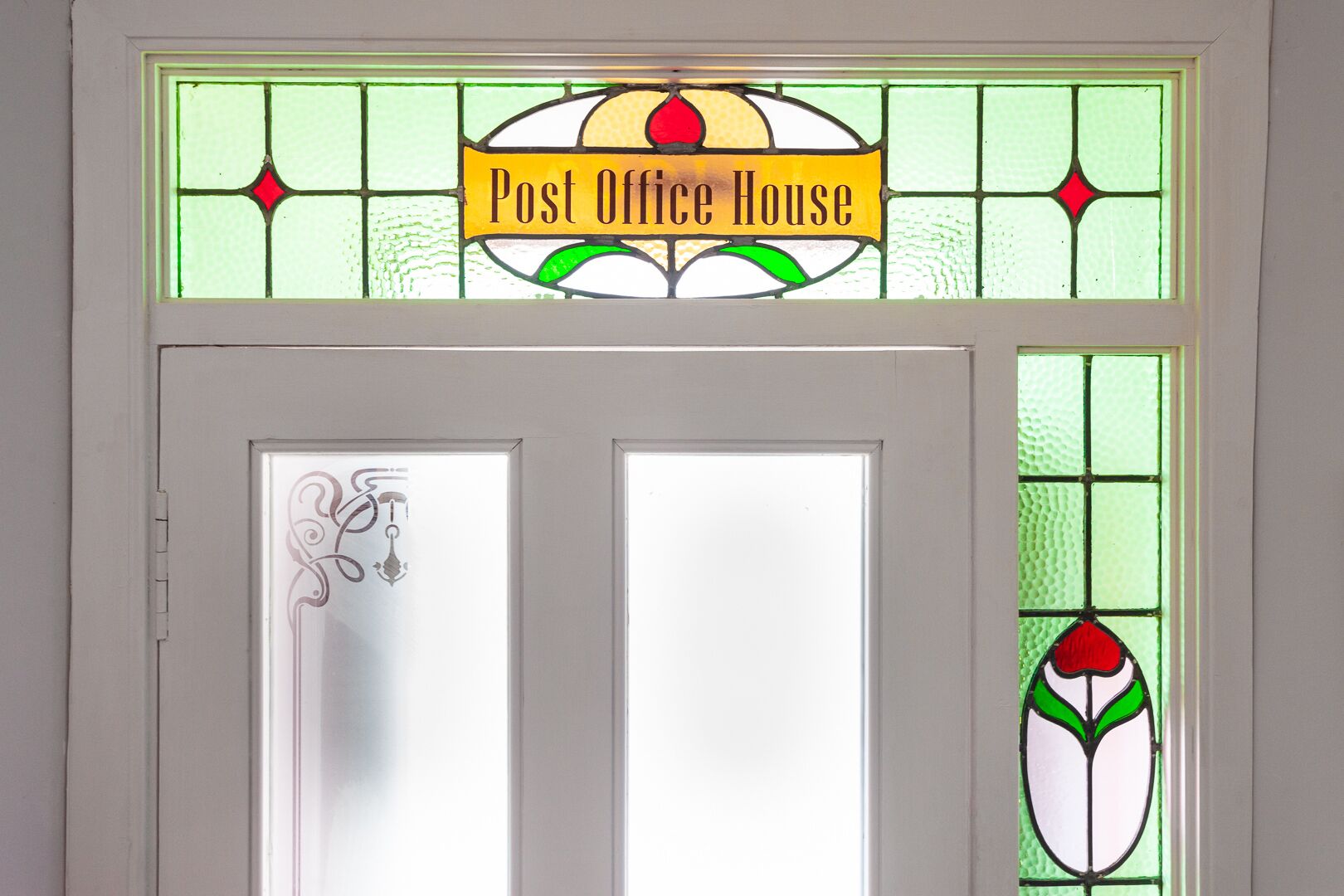 A door with a stained glass sign reading 'Post Office House' and a decorative glass panel with a floral design.