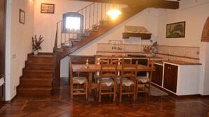 Un escalier en bois mène à une salle à manger, avec une cuisine en arrière-plan.