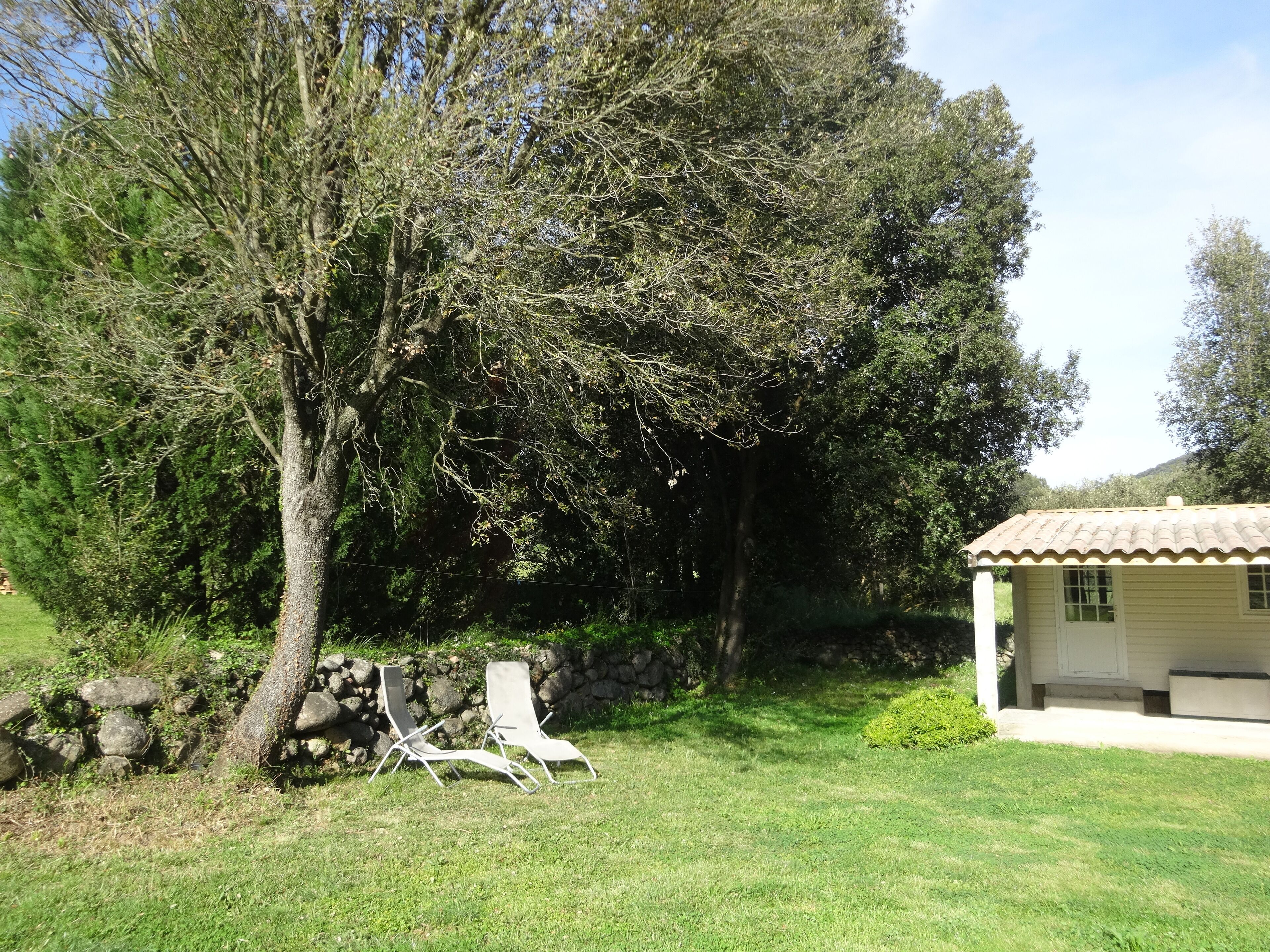 A house with a tiled roof, a stone wall, and two lawn chairs.