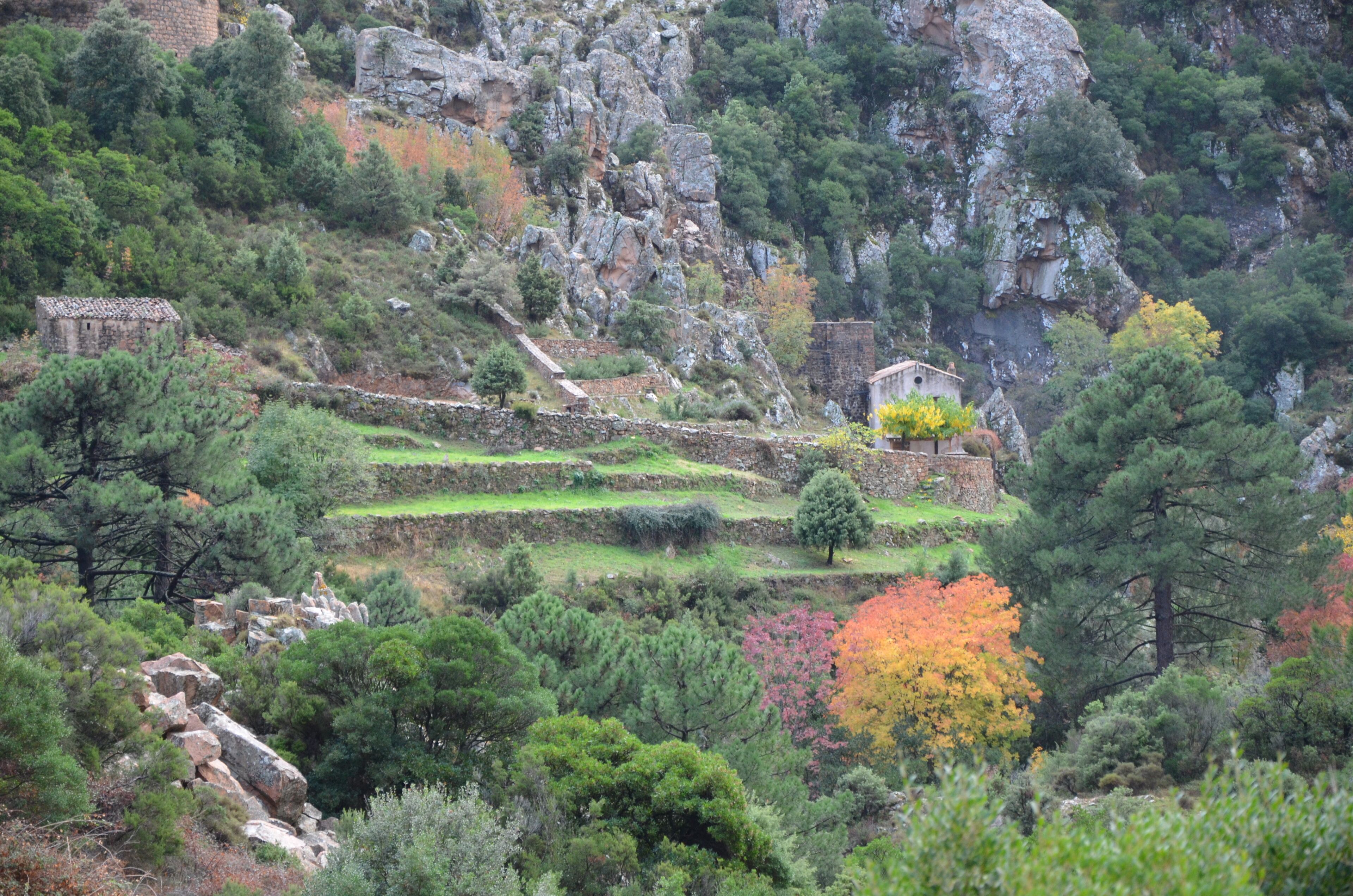 A mountainous landscape with terraced fields, a stone building, and a small structure.