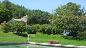 Ein Schwimmbecken mit Steinkante, umgeben von üppiger Vegetation und einem Steinhaus im Hintergrund.