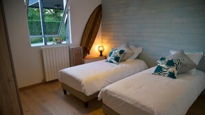 Een slaapkamer met twee bedden, een raam, een surfplank en een wandlamp.