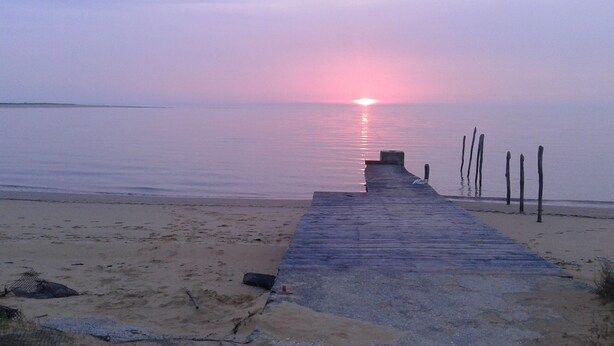 Eine hölzerne Mole führt zu einem ruhigen Strand bei Sonnenuntergang.