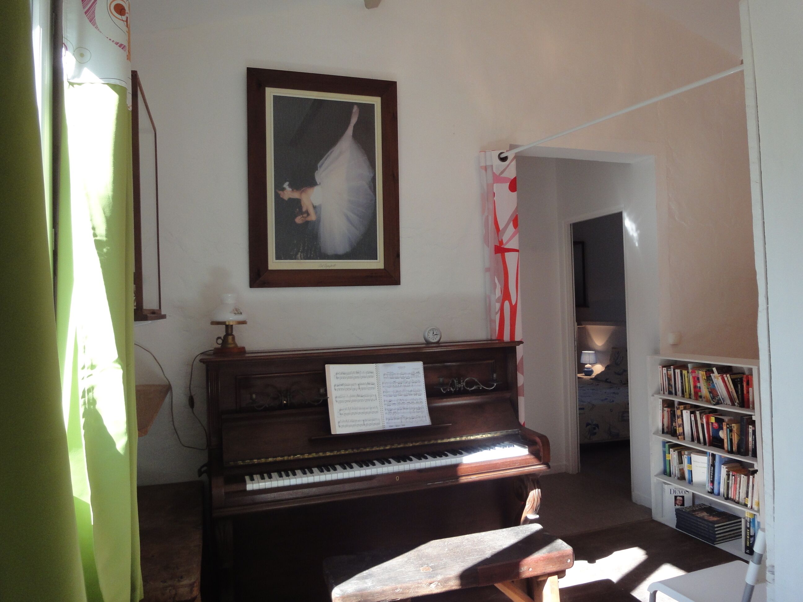 Ein Zimmer mit einem Klavier, einem Bücherregal und einem Gemälde an der Wand.