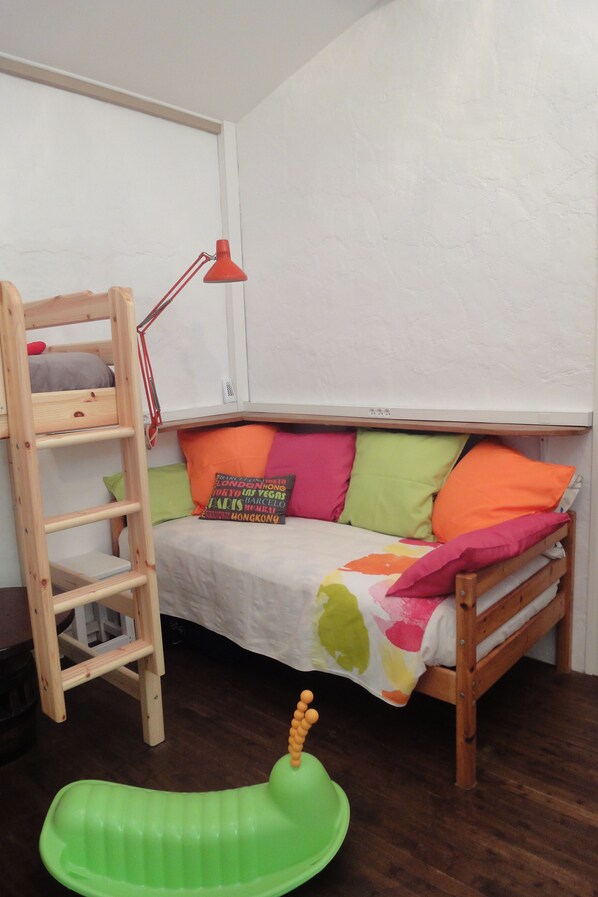 A bunk bed with a ladder, a small desk, a red desk lamp, and colorful pillows.