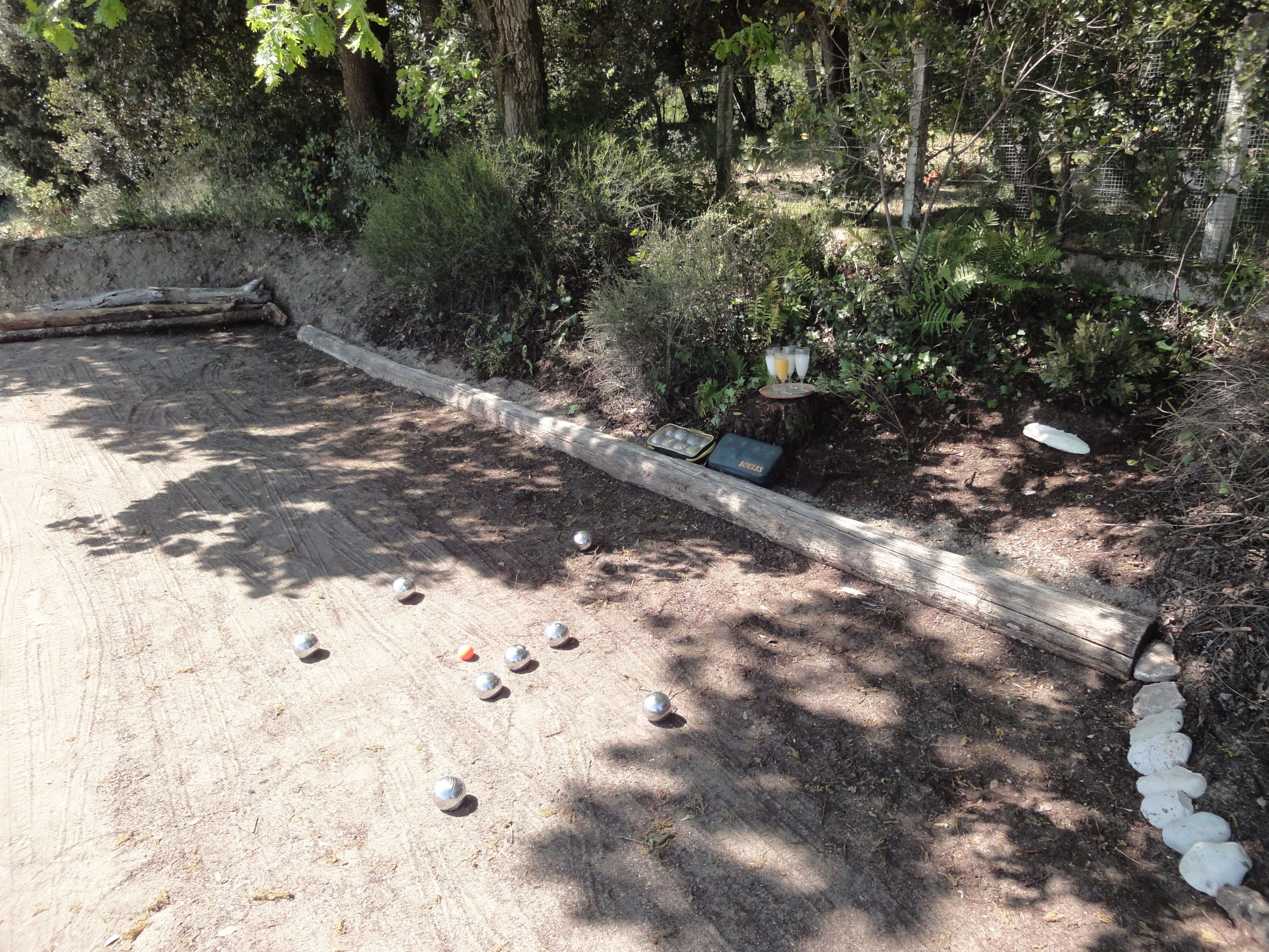 Un espacio al aire libre con arena, una cerca de madera, una mesa pequeña con un vaso y varias esferas metálicas.