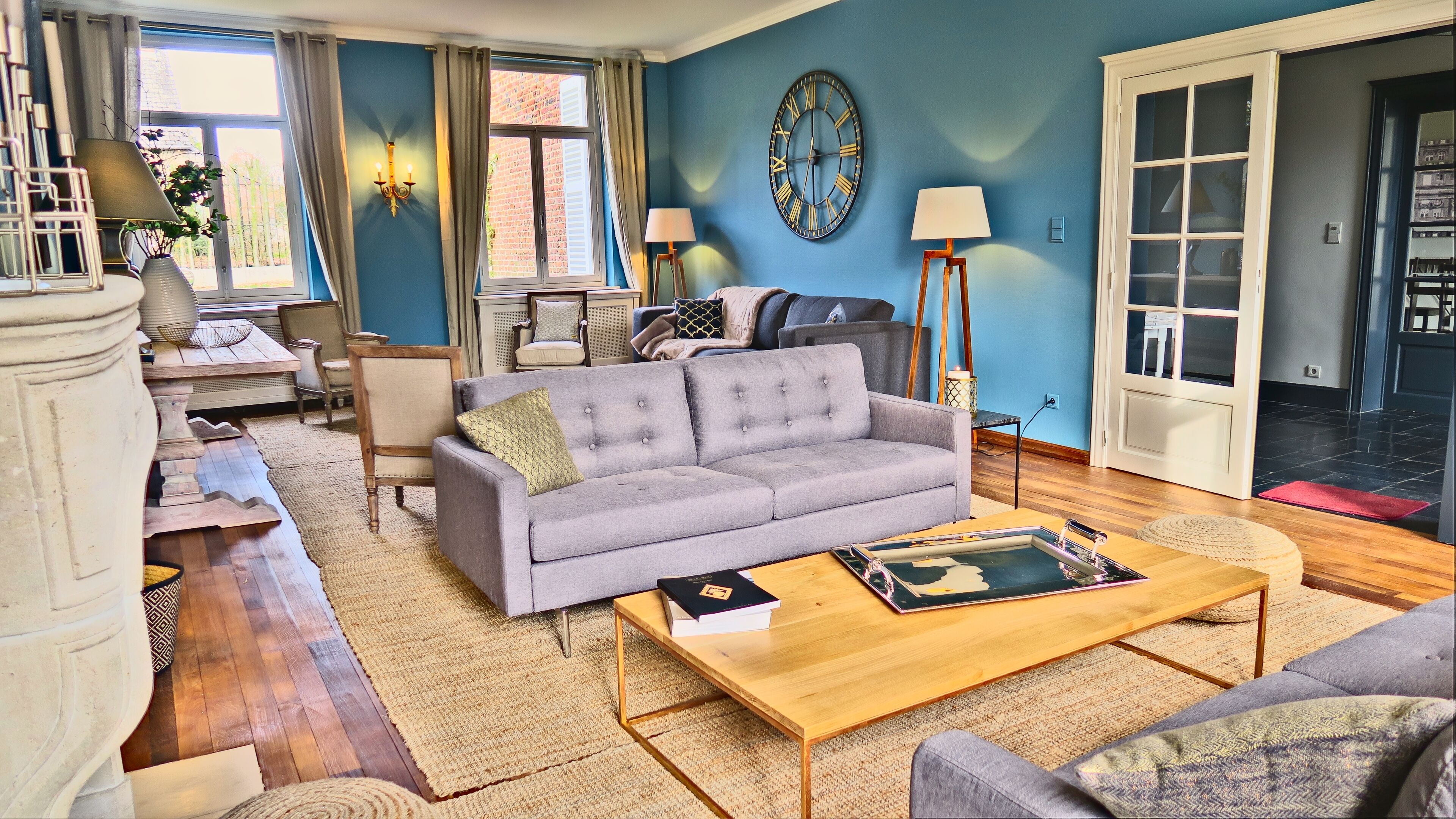 Ein Wohnzimmer mit einem grauen Sofa, einem Holztisch und einer großen Wanduhr.