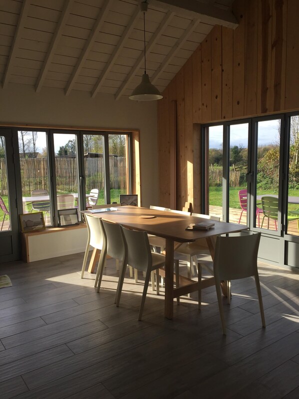 A spacious dining area with a large wooden table and chairs, large windows, and a view of the outdoors.
