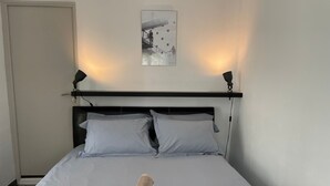 Siististi pedattu sänky, jossa on pyyhe, musta pääty ja seinälle ripustettu taulu.