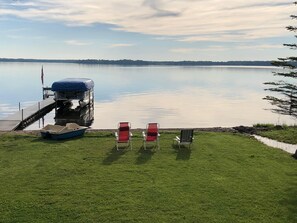 A grassy area with a dock and a truck, overlooking a calm lake with a distant shoreline. - Lake Front Cabin On Sturgeon Lake!  Amazing sandy beach for swimming! (Sturgeon Lake)