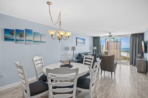 A dining area with a round table, white chairs, and a chandelier. There are paintings on the wall and a view of the ocean through large windows. - Unobstructed Ocean View ,2 bedroom , 12th Floor Pelican Beachfront  (destin)