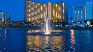 A hotel with a large fountain in front, surrounded by water reflecting lights.