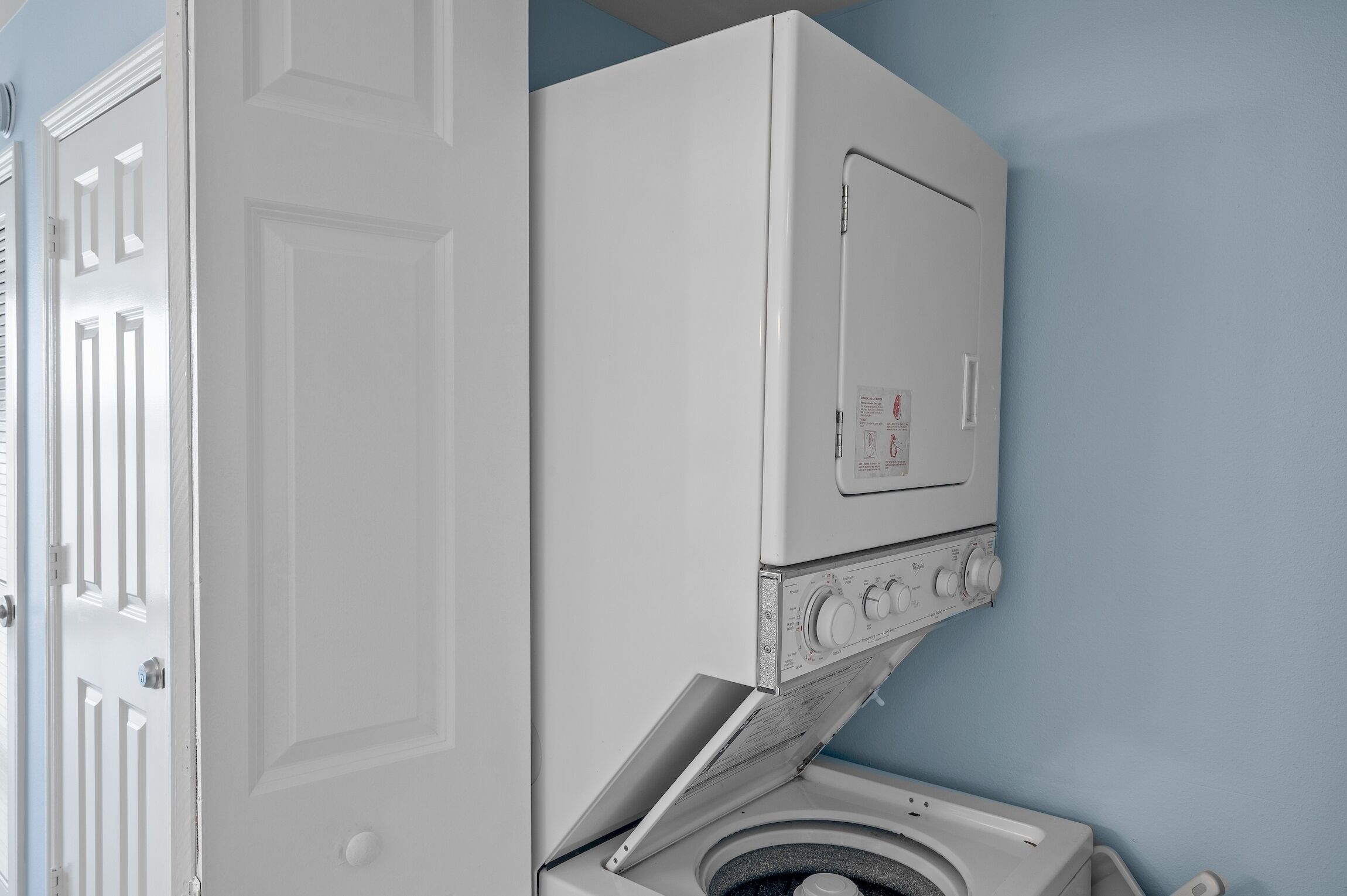 A front-loading washing machine and dryer in a laundry room with a white door and blue walls.