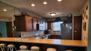 Una cocina con armarios de madera, una isla central con taburetes, un refrigerador y un microondas.