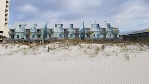 Un hotel frente a la playa con edificios de varios pisos, balcones y una playa arenosa al frente.