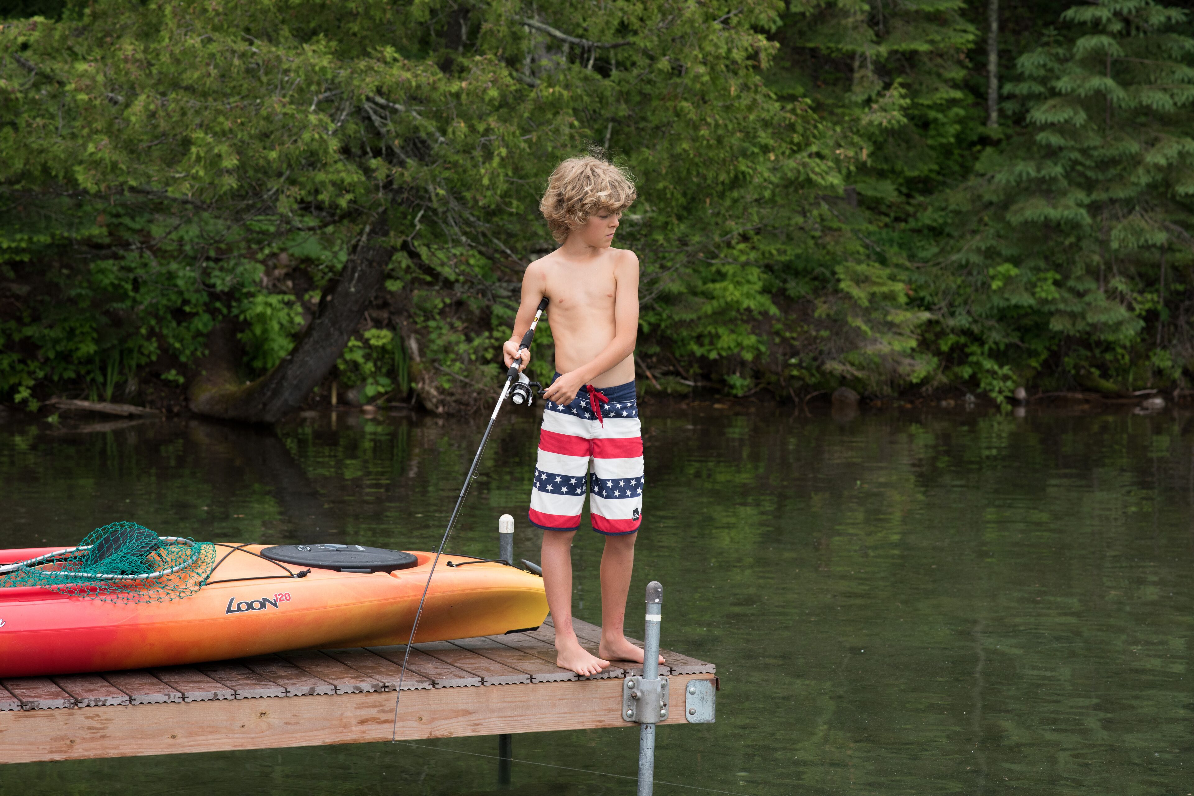 A wooden dock with a kayak and fishing rod.