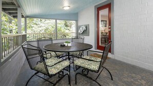 Un patio techado con una mesa redonda y sillas, una puerta con marco rojo y un muro de ladrillo blanco.