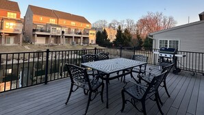 Eine Terrasse mit einem Metalltisch und Stühlen, mit Blick auf ein Wohngebiet mit Häusern und einem Gewässer.