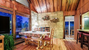 Un comedor de madera con pared de piedra, una mesa con sillas, un banco y un televisor.