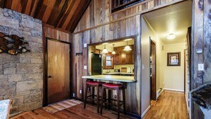 Una cocina rústica con paredes de madera, un detalle de pared de piedra y una zona de bar con taburetes.