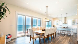 A modern kitchen with a large island, a dining area with six chairs, and a view of the ocean through large windows. - Gulf front home on North Cape, outdoor kitchen, elevator @ lots of beach gear (Port St Joe)