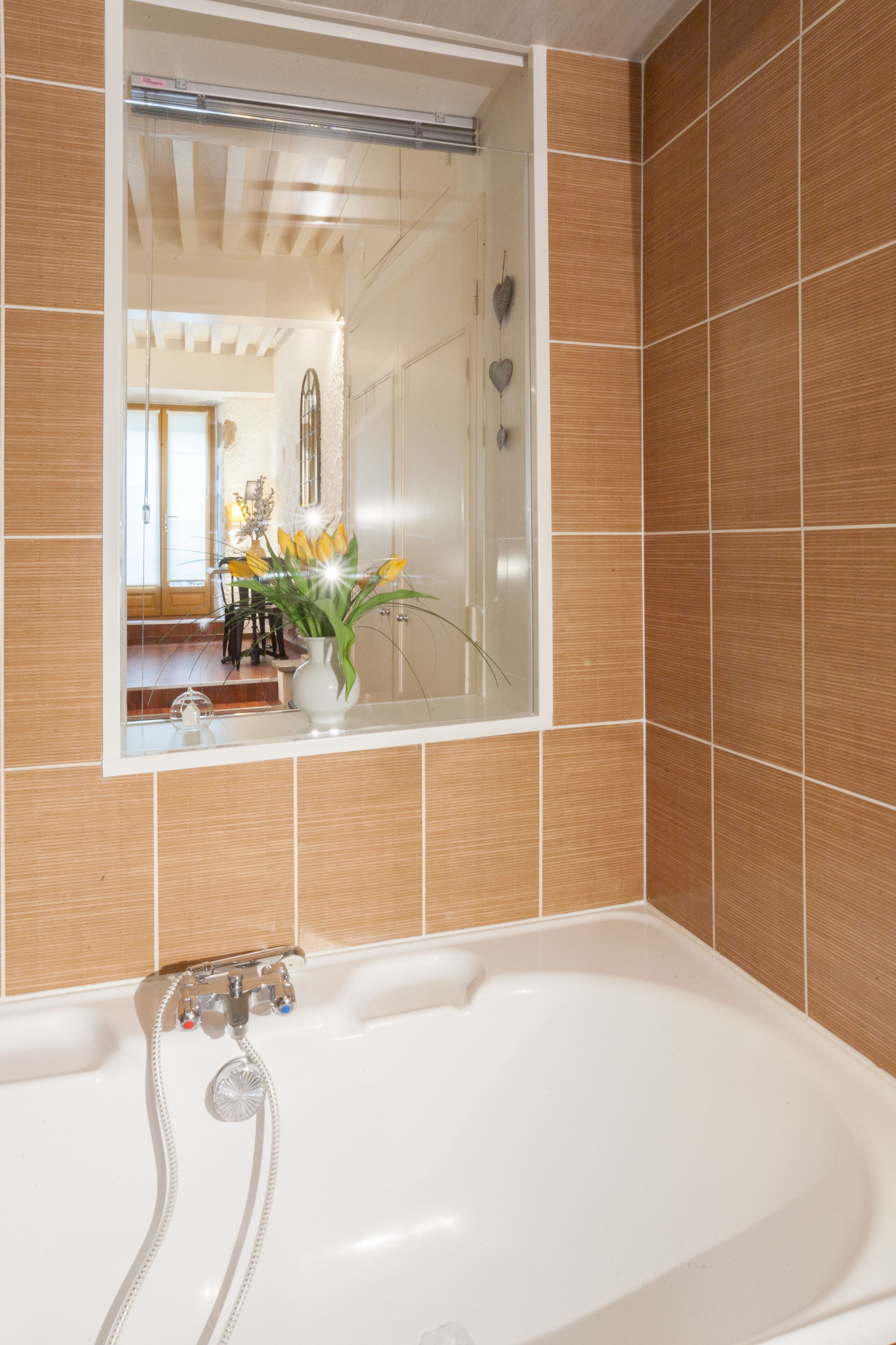 Une salle de bain avec une baignoire, un miroir et une plante en pot ornée de fleurs jaunes.
