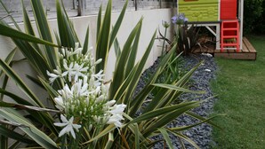 Ein Garten mit einem hölzernen Spielhäuschen, einem roten Stuhl und weißen Blumen.