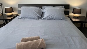 A neatly made bed with two pillows and two towels, flanked by two bedside tables with lamps, in a modern hotel room. - Bright apartment with garden - Linen, towels and final cleaning provided (Saint-Palais-Sur-Mer)