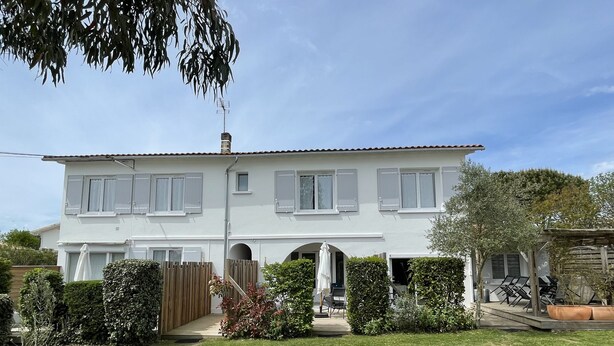 A two-story house with a white exterior, multiple windows with shutters, a wooden fence, and a well-maintained lawn. - Bright apartment with garden - Linen, towels and final cleaning provided (Saint-Palais-Sur-Mer)