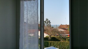 A room with a window overlooking a residential area, featuring a view of houses and a clear sky. - Bright apartment with garden - Linen, towels and final cleaning provided (Saint-Palais-Sur-Mer)